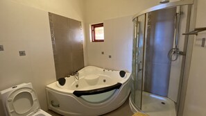 A modern bathroom with a jacuzzi, a glass-enclosed shower, and a toilet.