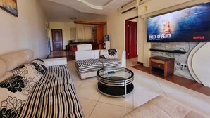 Una sala de estar con un sofá, una mesa de centro y un televisor mostrando 'TREES OF PEACE'.