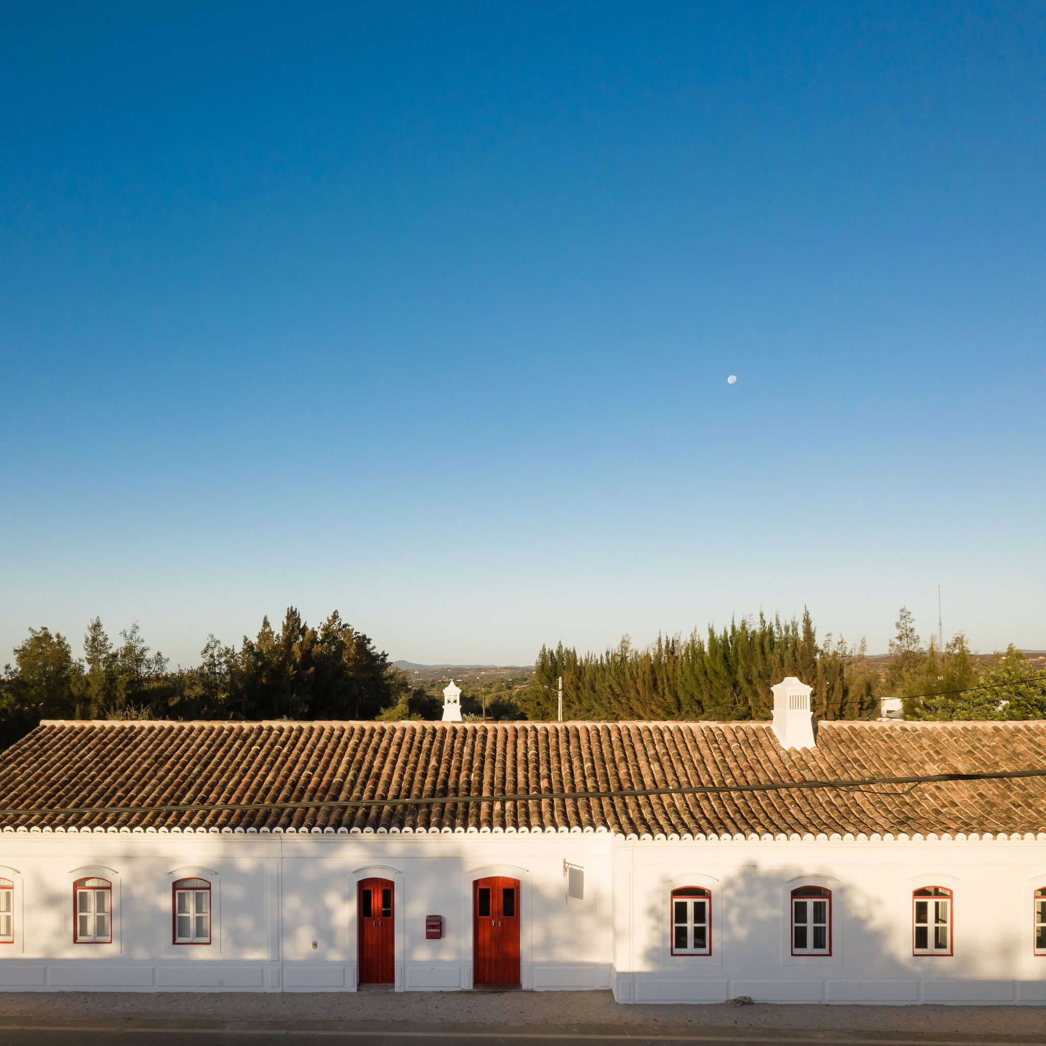 A white building with a tiled roof and multiple windows with red frames.