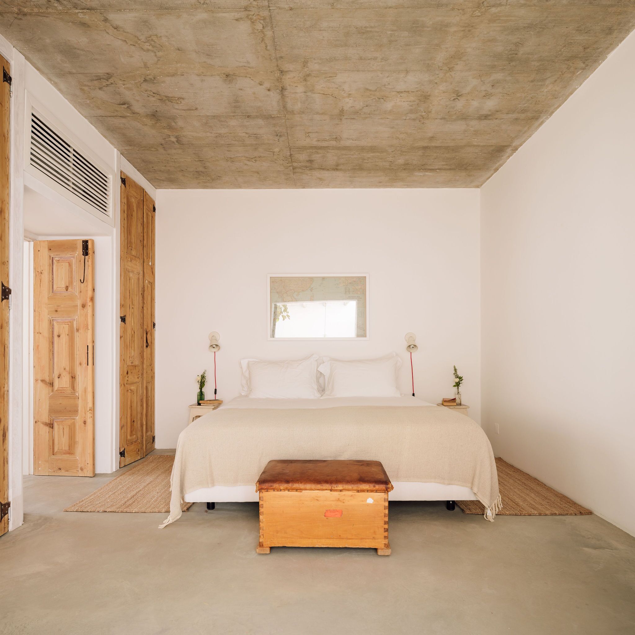 A minimalist bedroom with a large bed, wooden doors, and a concrete ceiling.