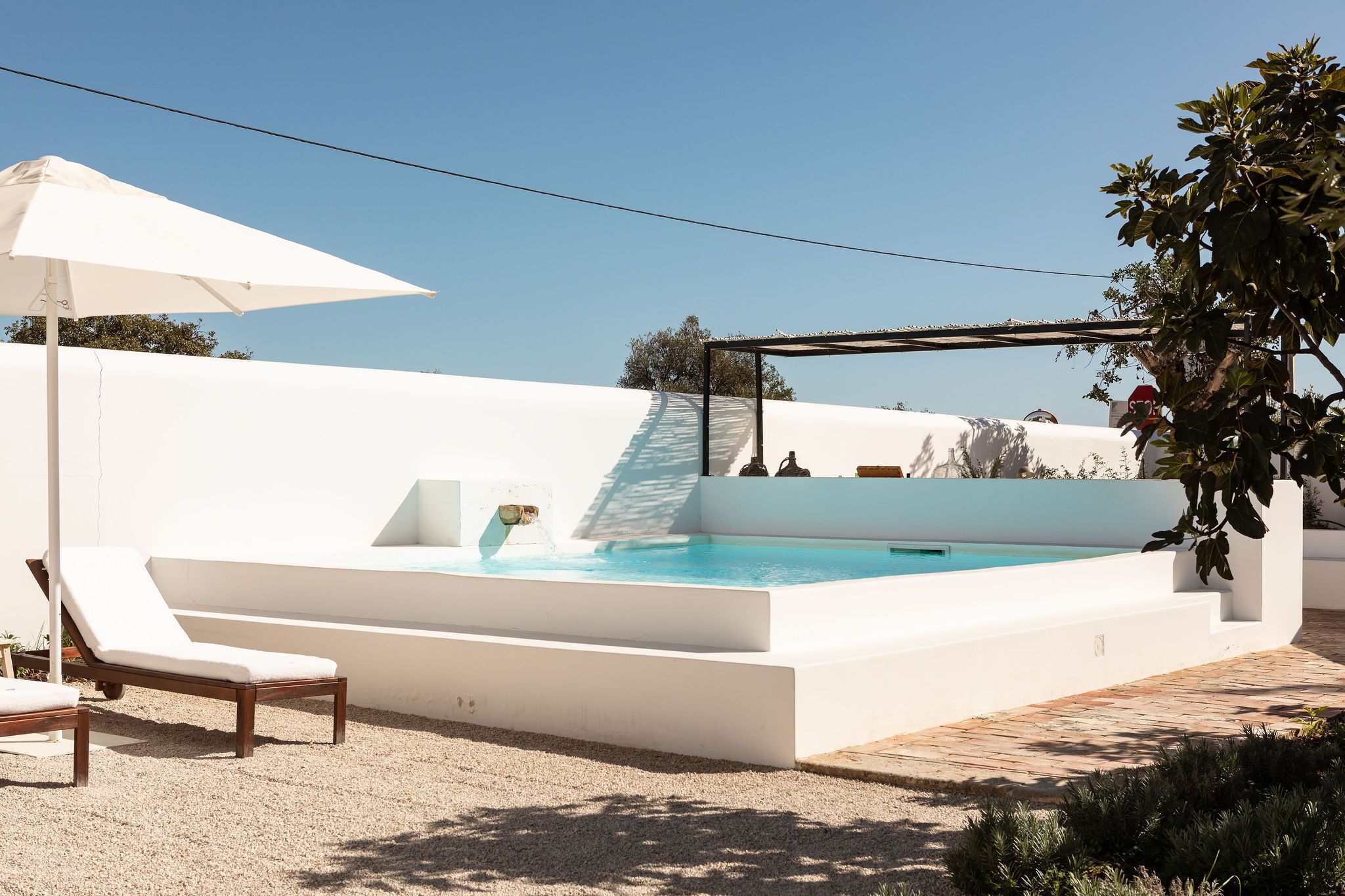 Un espace piscine extérieur moderne, avec une piscine blanche, un fauteuil de relaxation et une pergola dotée d’un parasol.