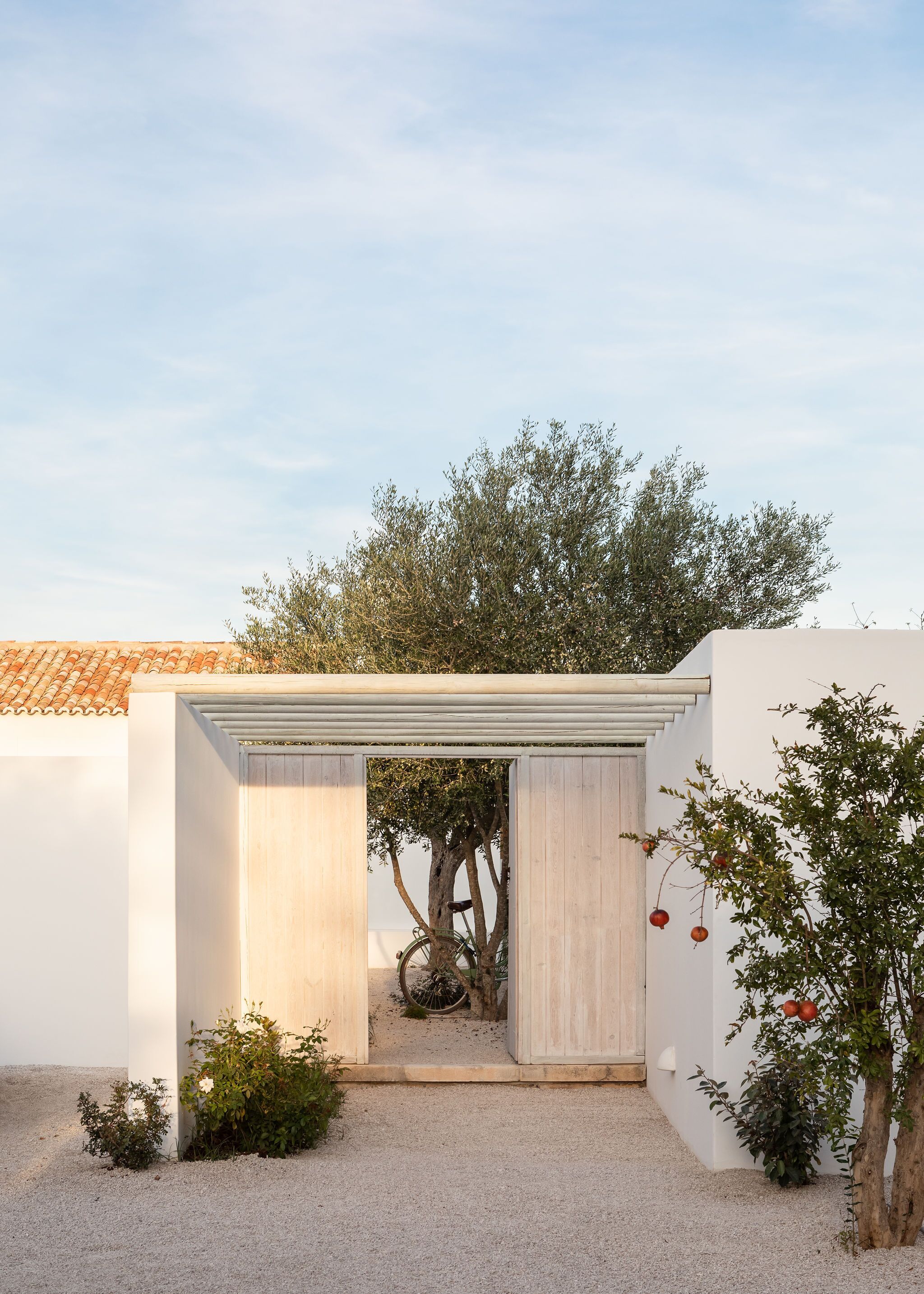 A white building with a tiled roof, a wooden door, and a gravel ground.