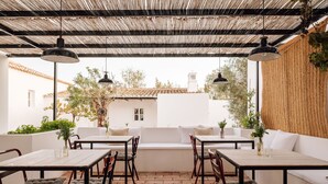 An outdoor patio with white furniture, including tables and a sofa, under a metal roof. - Hospedaria (Tavira)