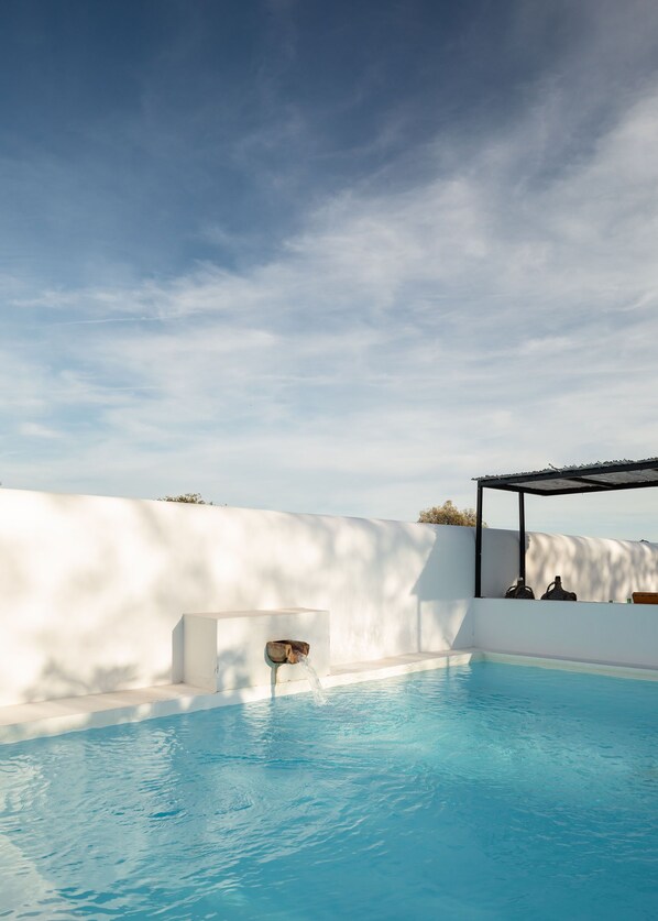 A swimming pool with a white wall and a pergola structure.