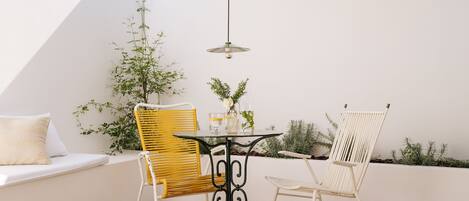 A cozy outdoor seating area with a round table, two chairs, a hanging light, and a woven ceiling.