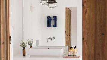 A modern bathroom with a white sink, two pendant lights, a wooden door, and a small plant.