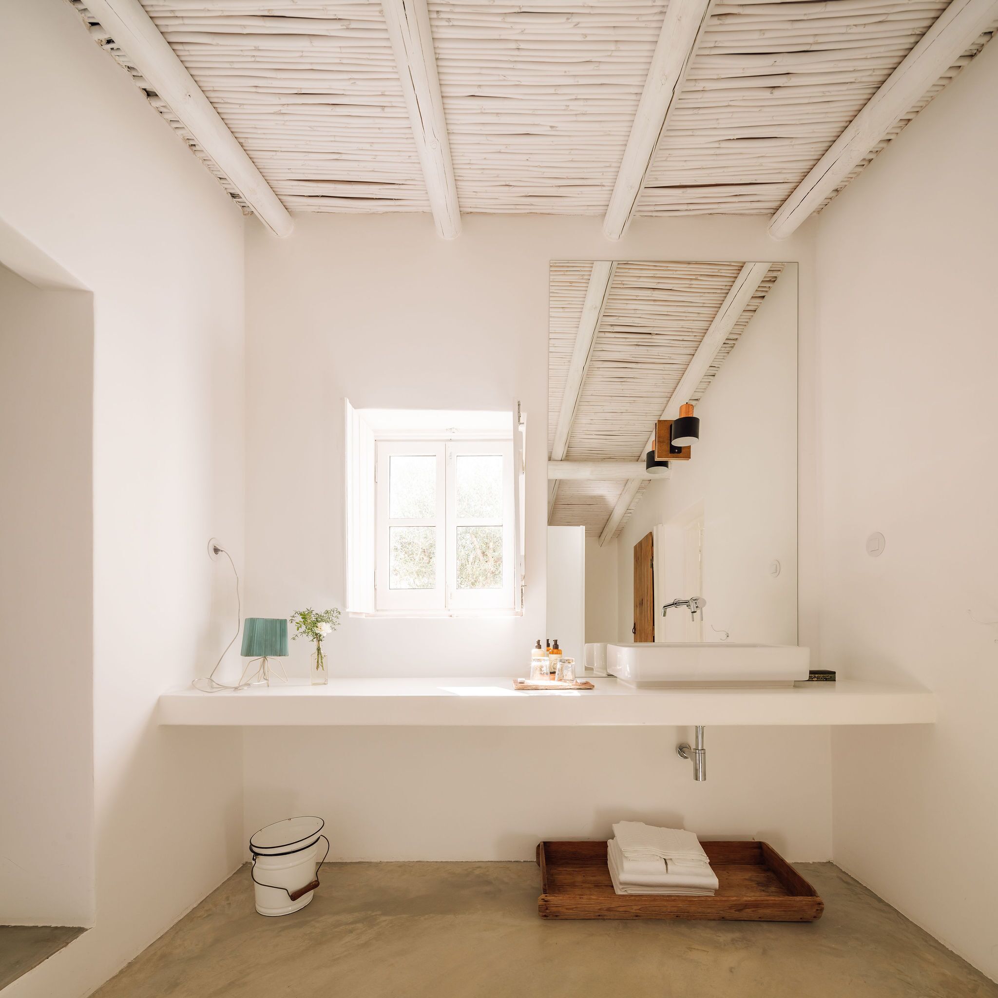 Ein minimalistisches Badezimmer mit großem Spiegel, weißem Waschtisch und einem Holztablett.
