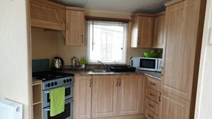 Eine kleine Küche mit Holzausstattung, einem Herd, einem Backofen, einer Mikrowelle und einem Fenster mit Jalousien.
