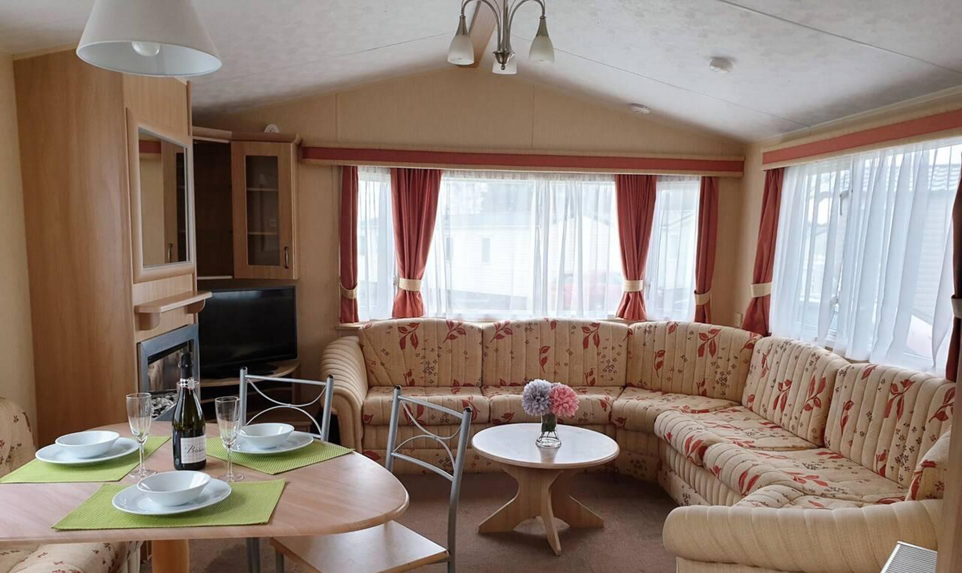 A cozy living area with a sofa, a television, a dining table with plates and glasses, and a small table with a vase of flowers.