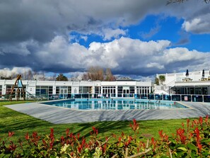 A swimming pool with a surrounding deck, a building with large windows, and a cloudy sky. - Charming 3-bed Holiday Home in Poole, Rockley Park (Poole)