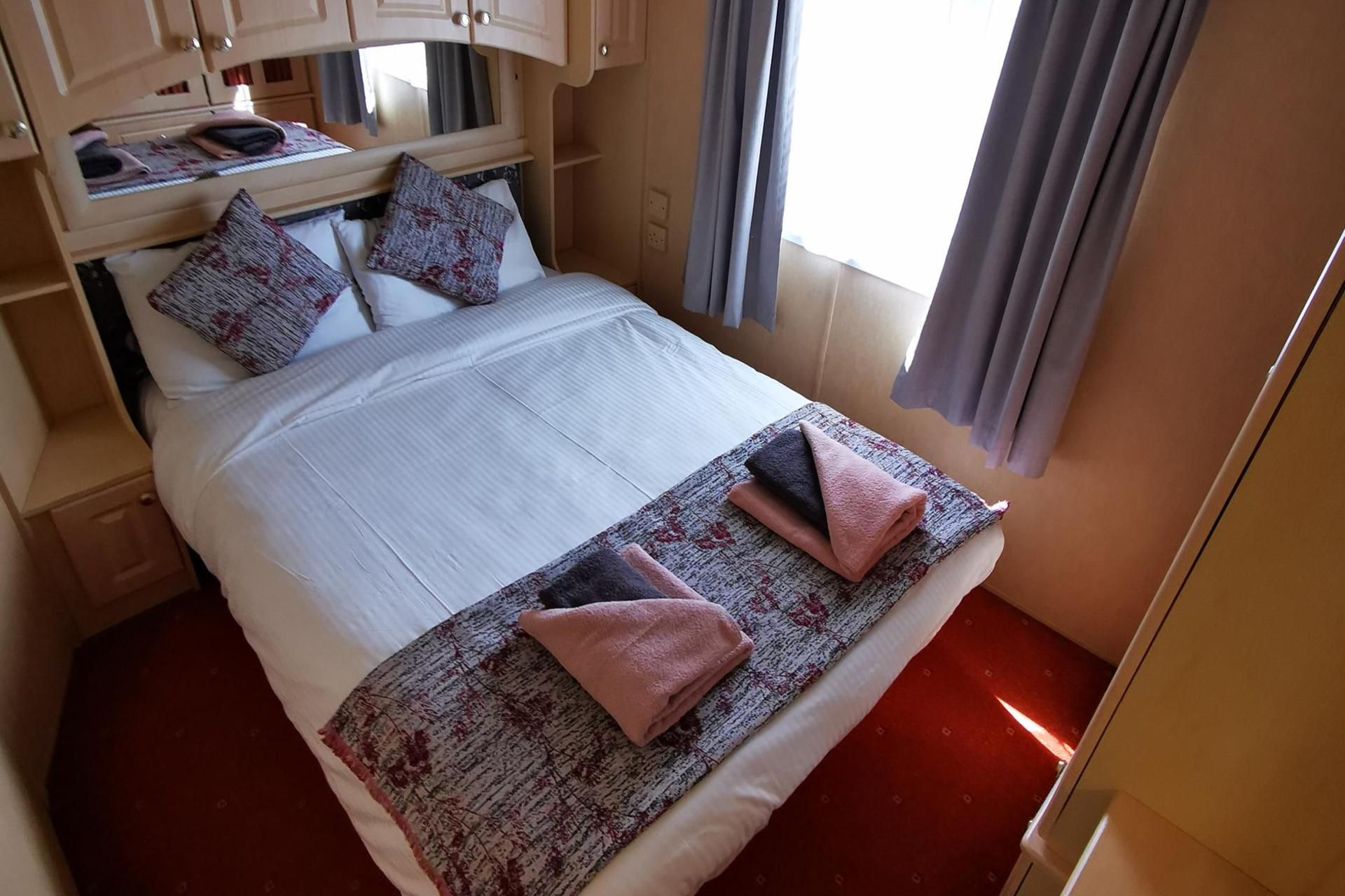A neatly made bed with a patterned bedspread and two folded towels.