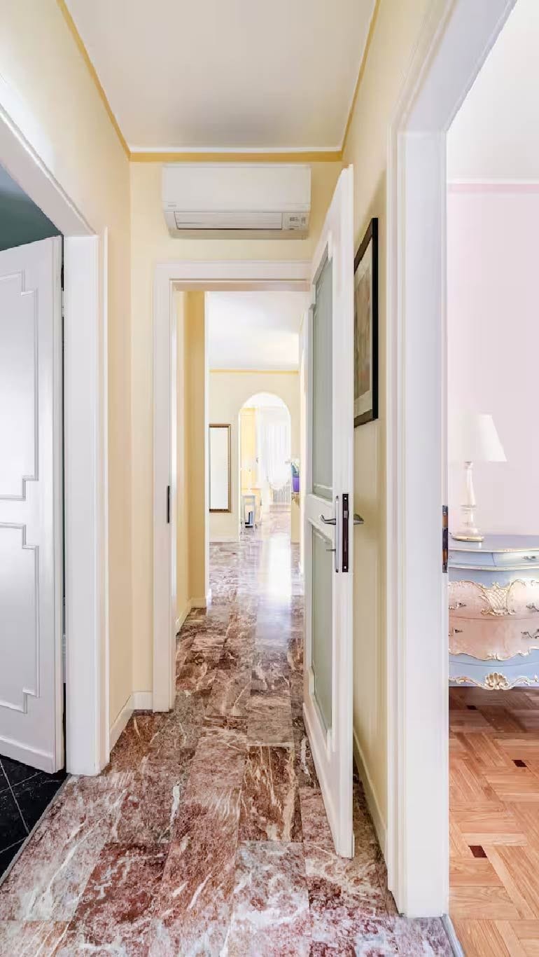 A hallway with a marble floor, white walls, and a door leading to another room.