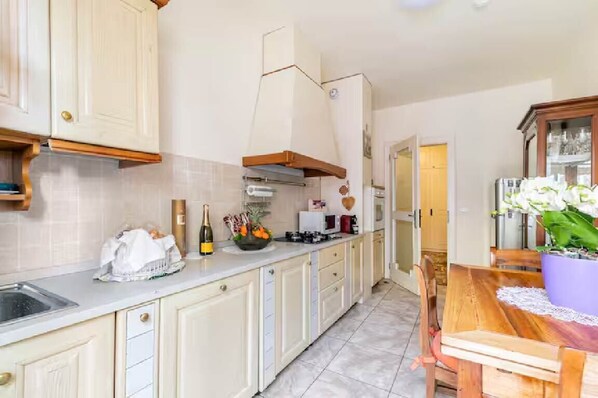 A kitchen with white cabinets, a wooden countertop, a dining table with chairs, and a potted plant.