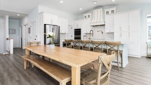 A modern kitchen with white cabinetry, a wooden dining table, and a built-in oven. - Beautiful 6 bedroom beach house with pool and elevator! Steps from the beach! (Oak Island)