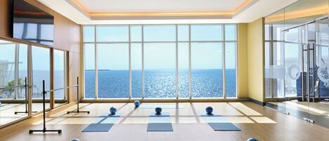 Amplia habitación con grandes ventanales con vistas al mar, colchonetas de ejercicio y balones de yoga dispuestos para actividades físicas.