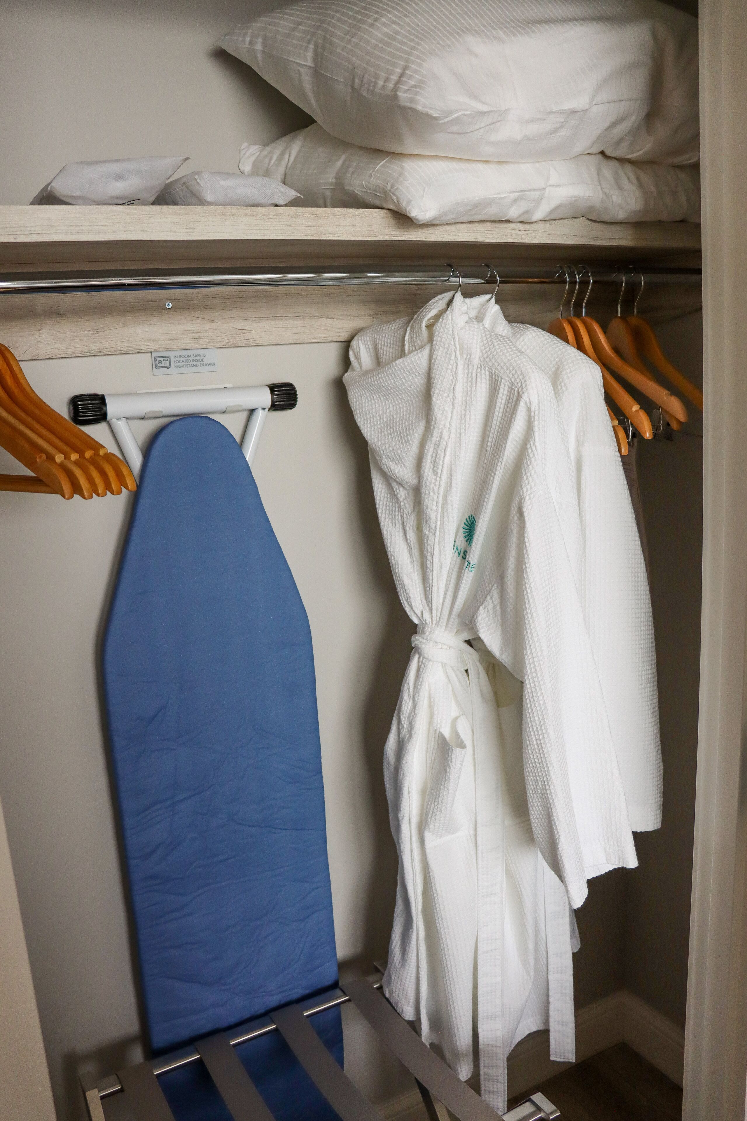 Un placard contenant des robes blanches soigneusement pliées et une planche à repasser bleue.