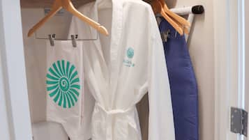 A closet with a wooden shelf, a white robe with a logo, a blue garment, and a white towel with a green logo.