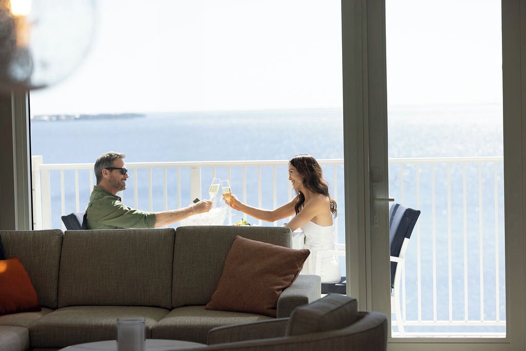 A couple toasting with wine glasses at a table with a view of the sea.