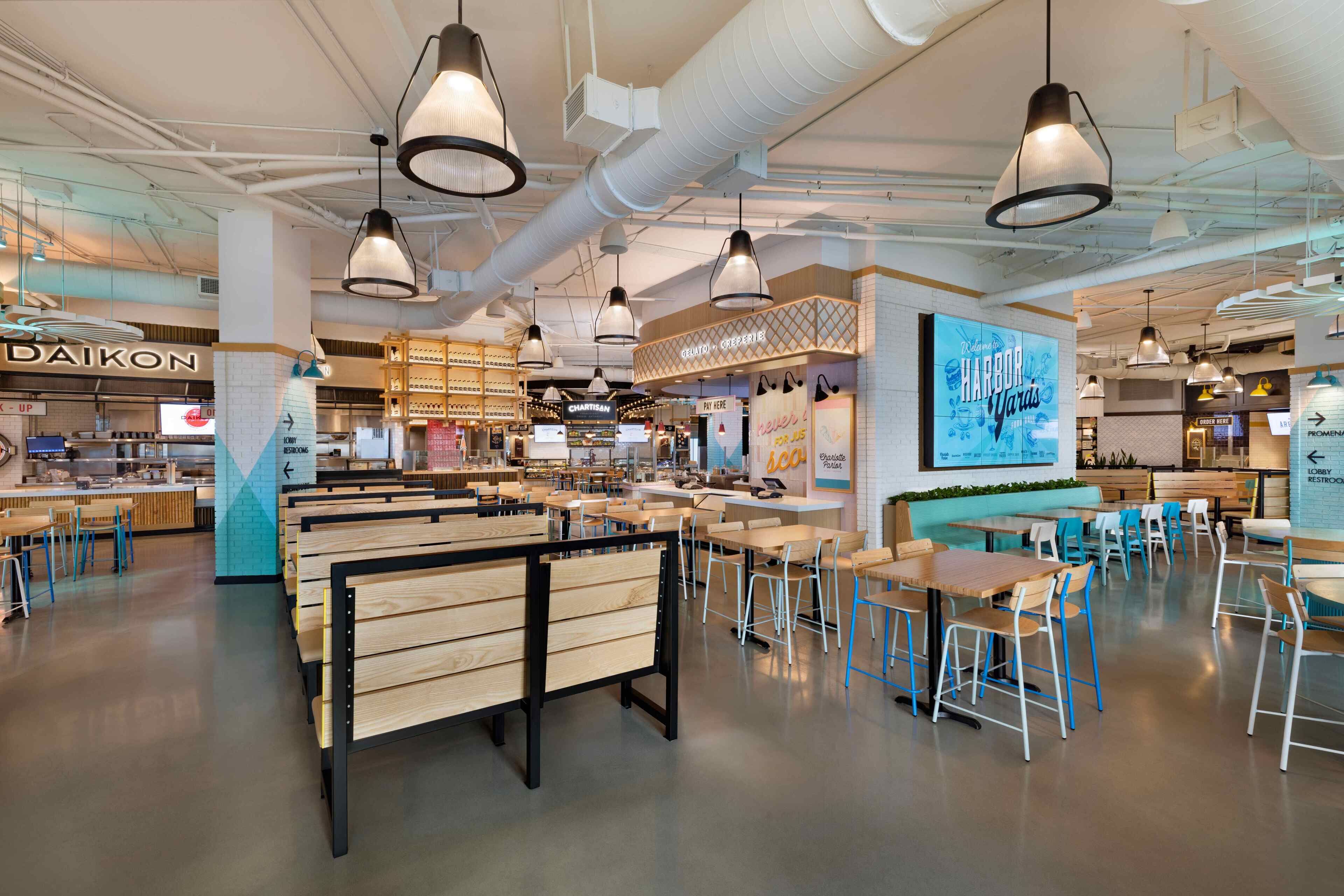 Un interior de restaurante moderno con bancos y mesas de madera, lámparas colgantes y una zona de barra visible.