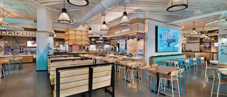 Un interior de restaurante moderno con bancos y mesas de madera, lámparas colgantes y una zona de barra visible.