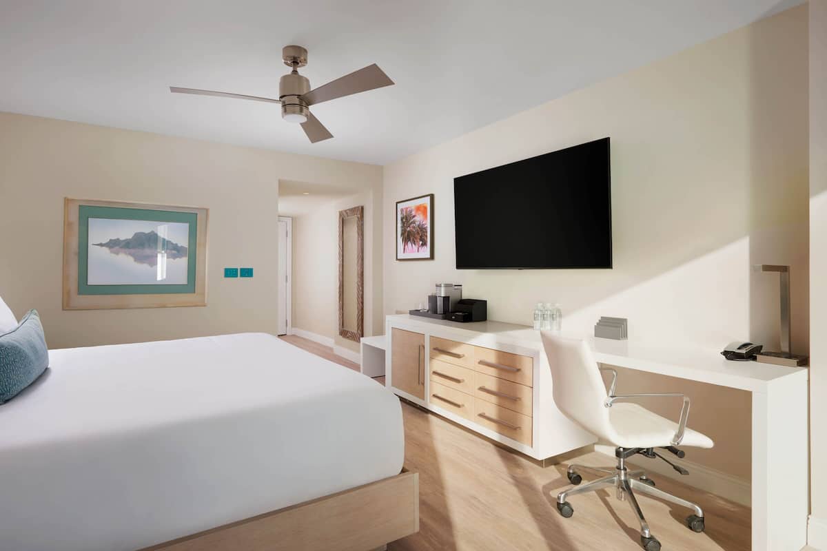 Een moderne hotelkamer met een groot bed, een bureau met stoel, een flatscreen televisie en een plafondventilator.