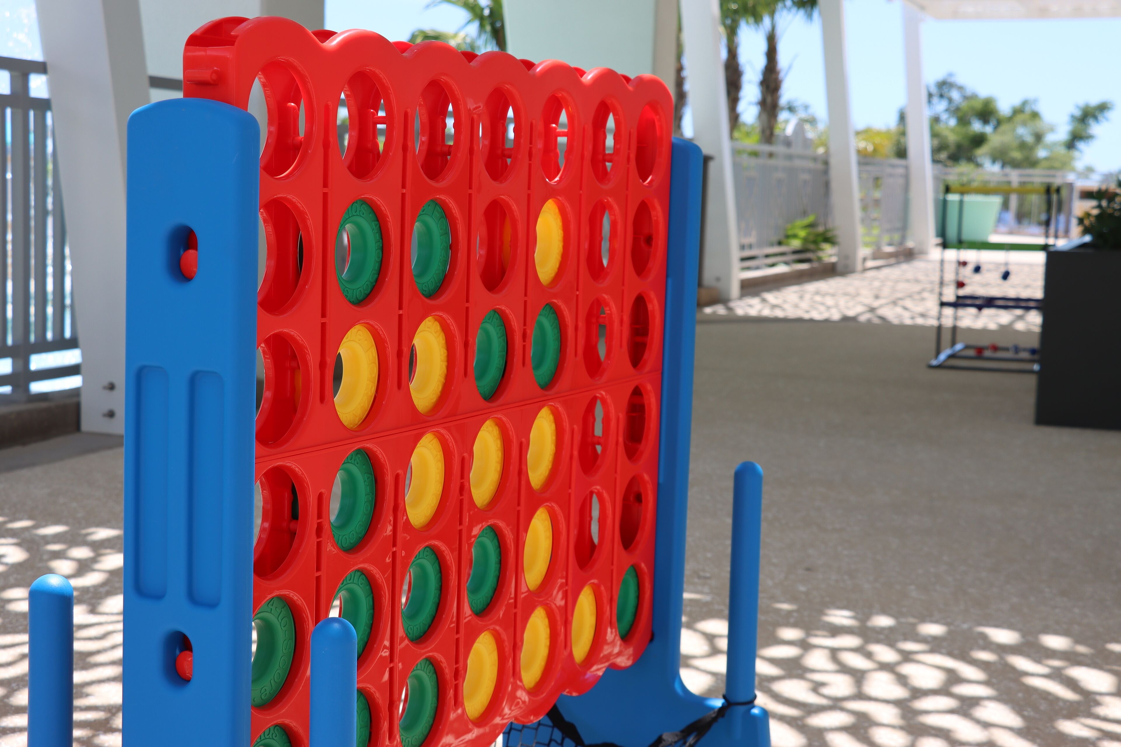 Un tablero de juego rojo y azul con agujeros, colocado al aire libre sobre una superficie pavimentada.
