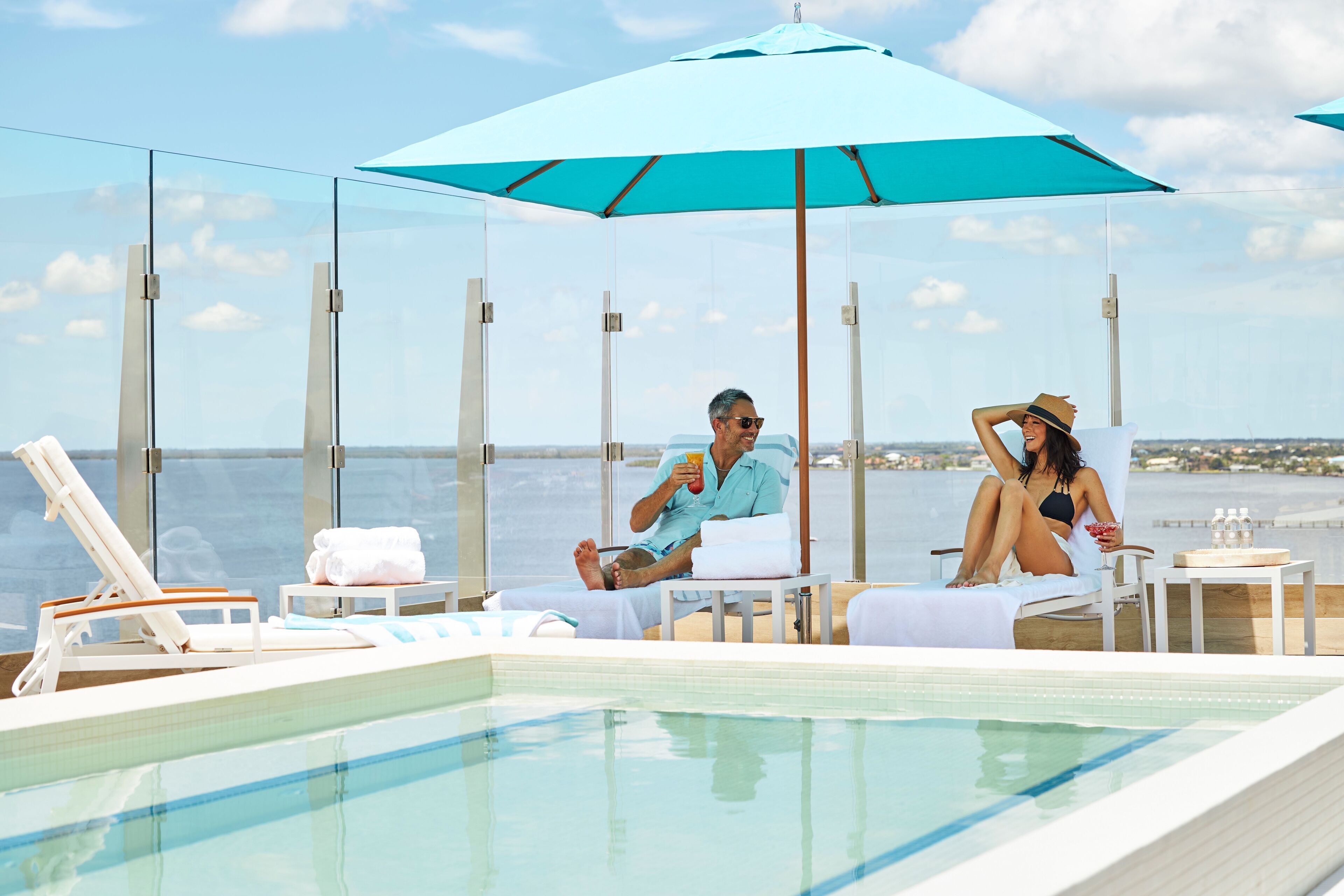 Een zwembadgedeelte met glazen loungeruimtes, een grote parasol en uitzicht op zee.