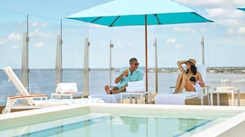 Een zwembadgedeelte met glazen loungeruimtes, een grote parasol en uitzicht op zee.