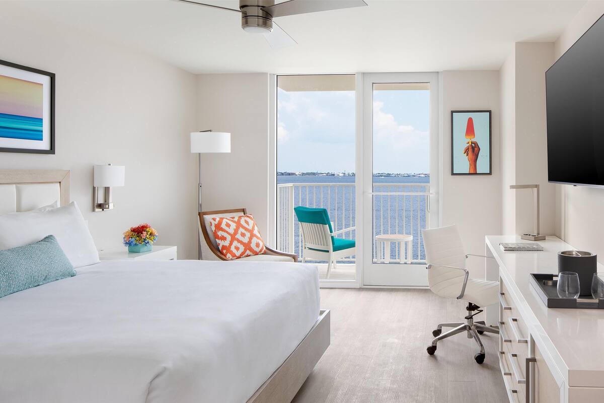 Une chambre d’hôtel avec un lit, un bureau, une chaise, une télévision et un balcon avec vue.
