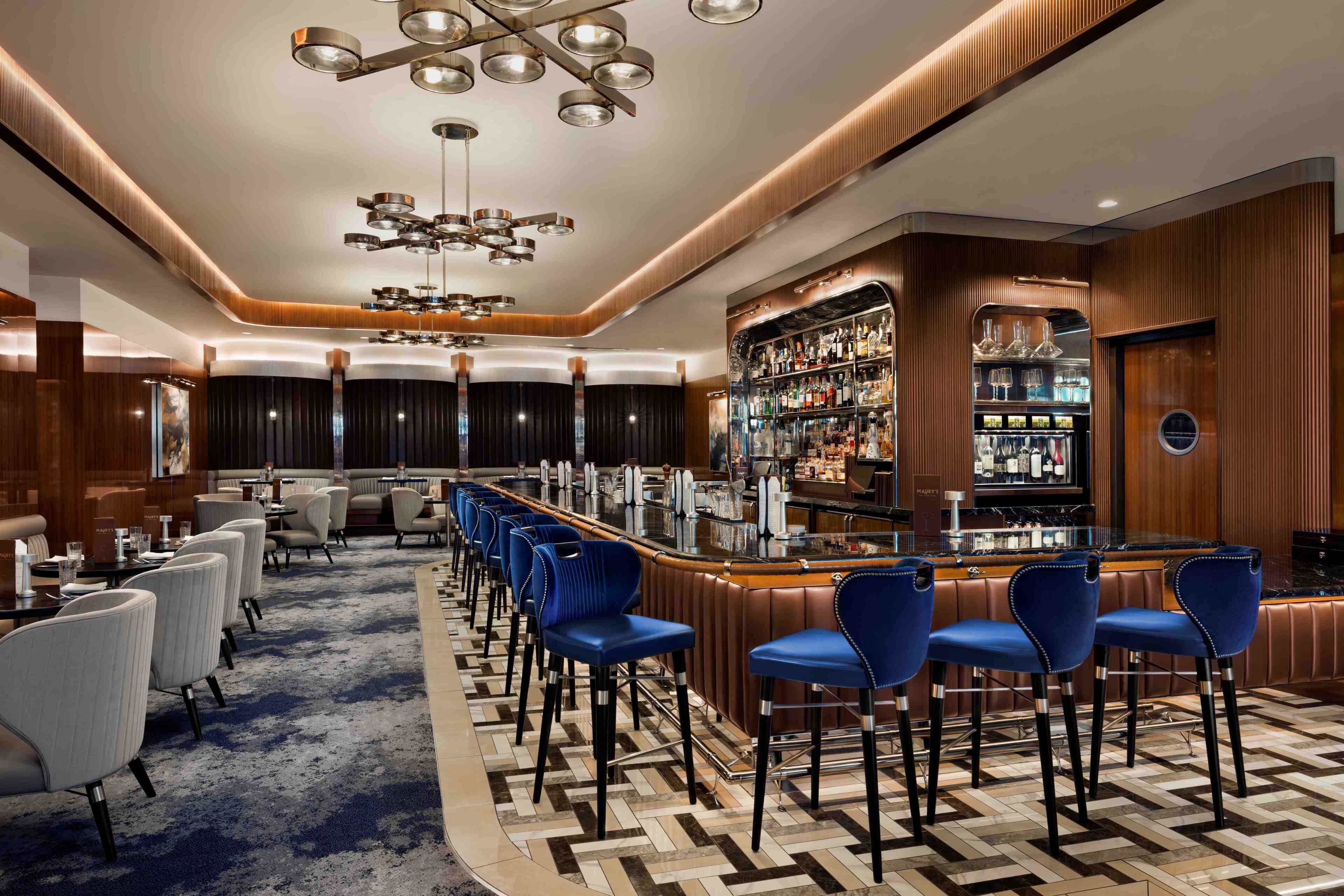 Un espace bar moderne avec un long comptoir, des tabourets de bar bleus et un bar bien approvisionné.