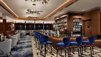 Uma área de bar moderna com um balcão comprido, banquetas azuis e uma variedade de bebidas.