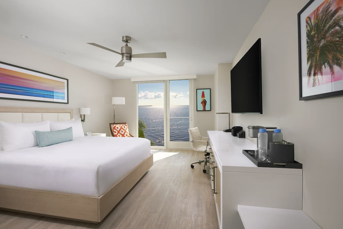 Een moderne hotelkamer met een groot bed, een bureau, een stoel, een televisie en uitzicht op de oceaan.