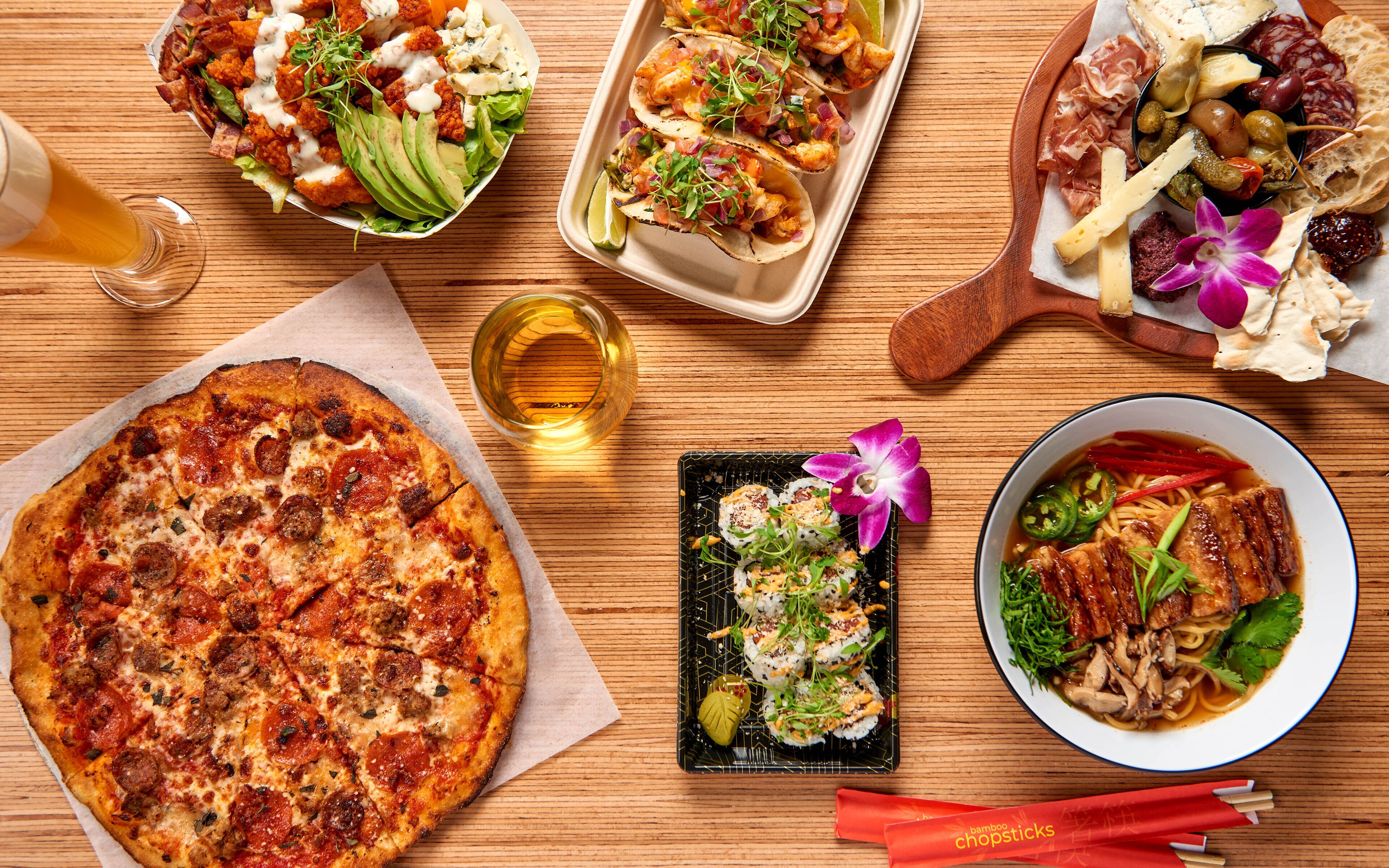 A variety of dishes including pizza, tacos, and sushi, arranged on a wooden table.