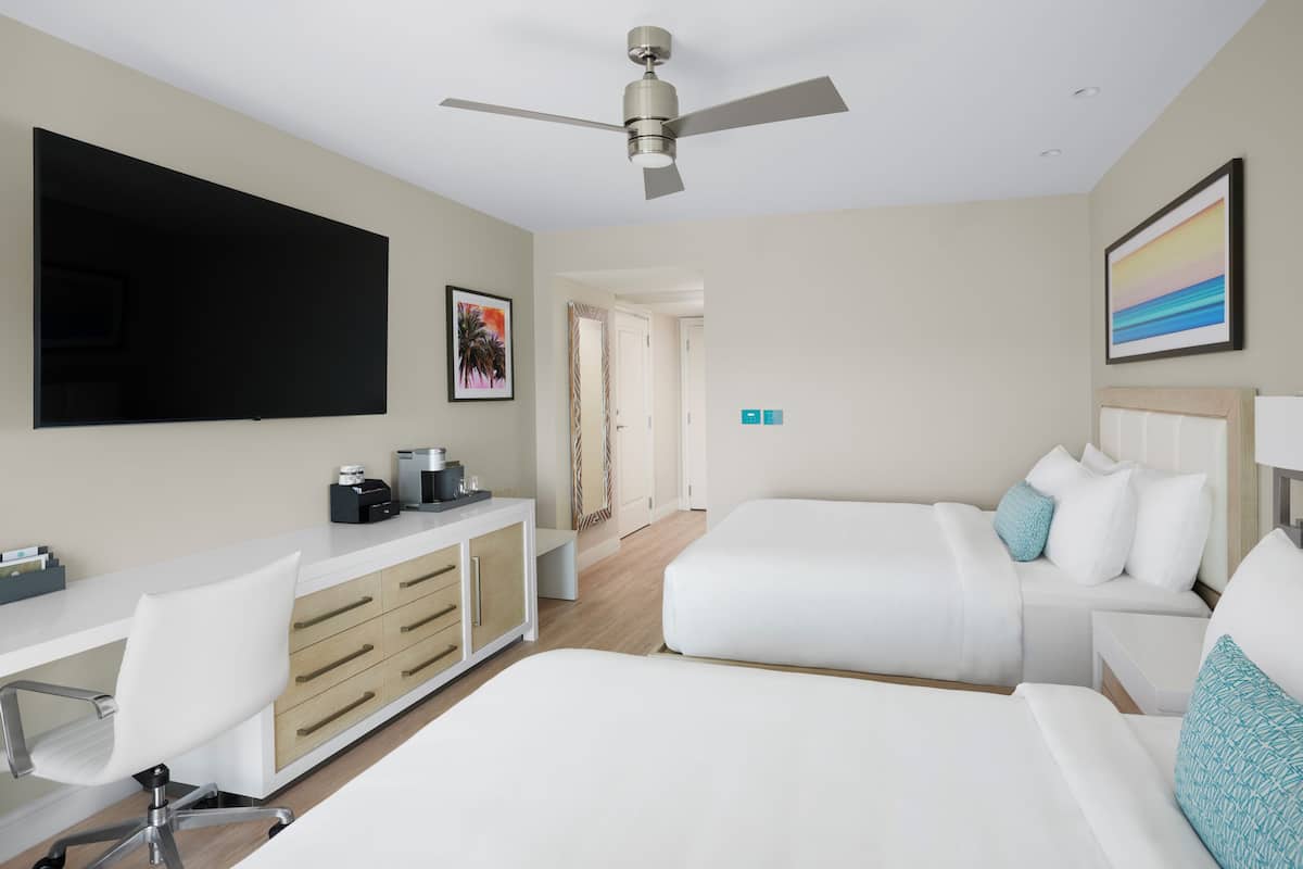 Hotelkamer met een bed, bureau met stoel, televisie, plafondventilator en schilderij aan de muur.