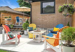 An outdoor patio with Adirondack chairs, a table, and hanging flower baskets. - The Maple Tree: Luxury Family Home (Burlington)