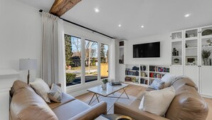 Un salon moderne avec des canapés en cuir, une table basse, une bibliothèque et un téléviseur fixé au mur.