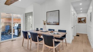 Un espace repas moderne avec une table en bois, des chaises bleues et une vue sur un patio aménagé avec du mobilier d’extérieur et un barbecue.