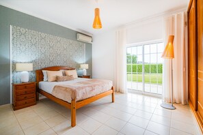 Relax in this serene bedroom with a large bed, patterned wallpaper, and a view of the surrounding green landscape.