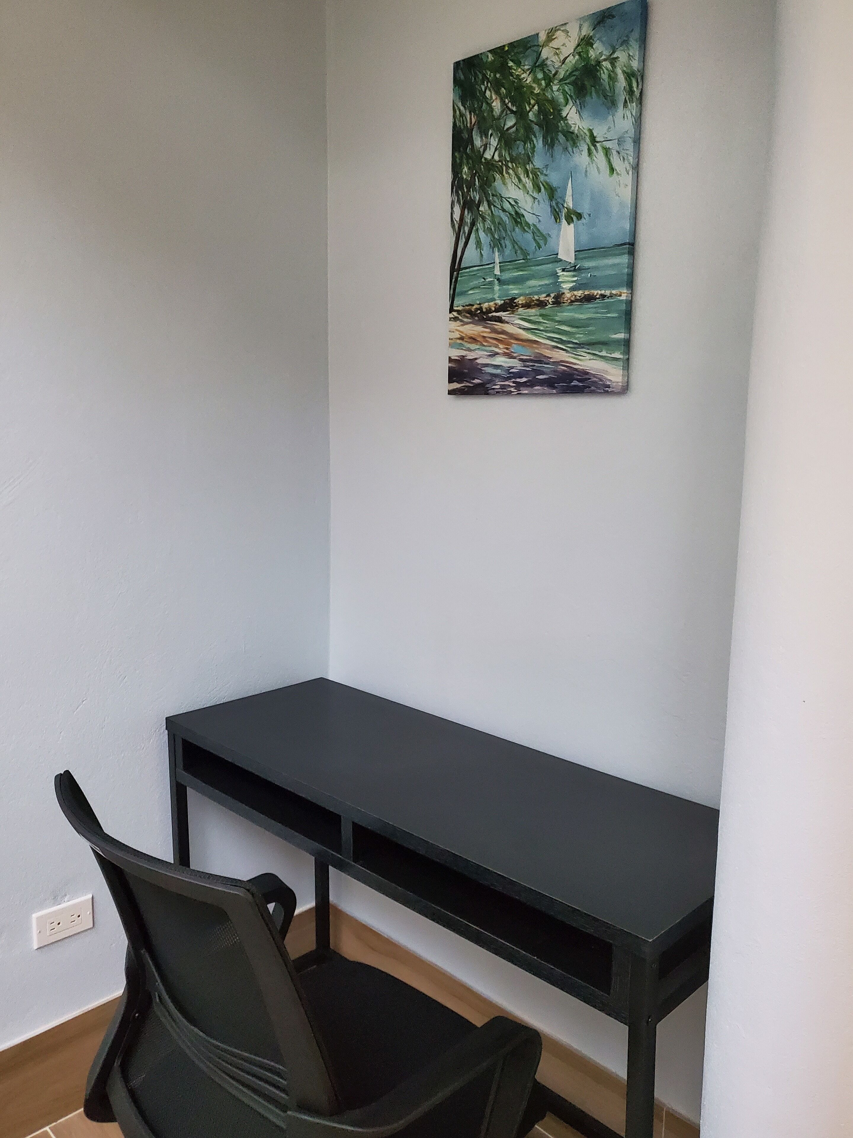 Una stanza con una scrivania nera, una poltrona da ufficio nera e un quadro raffigurante un faro su una spiaggia.