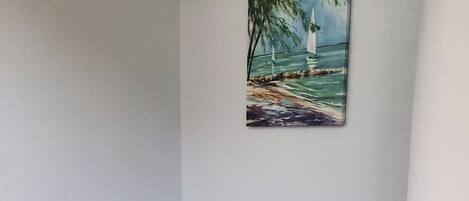 A room with a black desk, a black office chair, and a painting of a lighthouse on a beach.