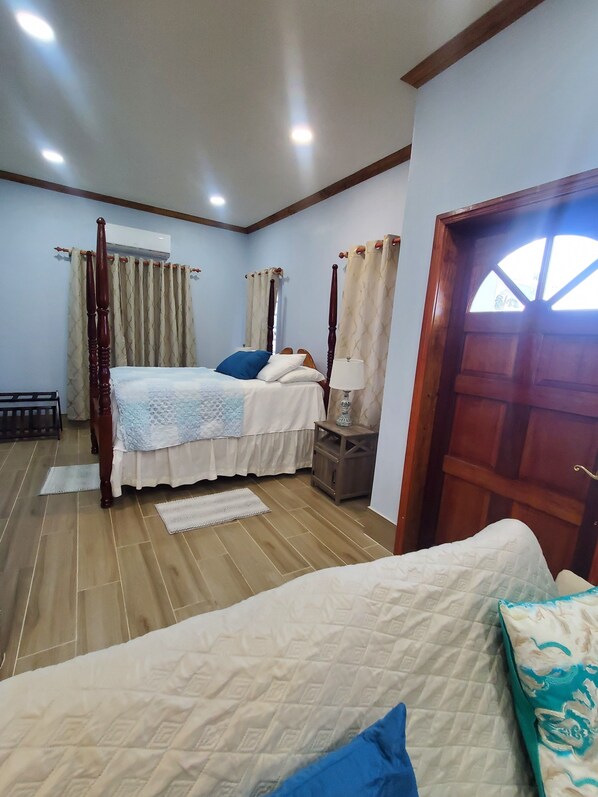A bedroom with a large bed, a smaller bed, wooden headboard, curtains, a nightstand, and a door.