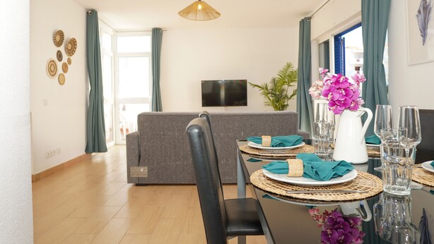 Un coin repas avec une table dressée pour quatre personnes, un canapé et un téléviseur en arrière-plan.