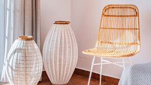A room with a white chair, two large vases, and a knitted blanket on a tiled floor.