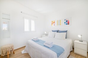 Une chambre avec un lit, des tables de chevet, un tabouret en macramé et des œuvres d’art murales.