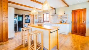 A modern kitchen with wooden beams, a central island, bar stools, and pendant lighting. - Casa Picota-Countryside & Pool (Boliqueime)