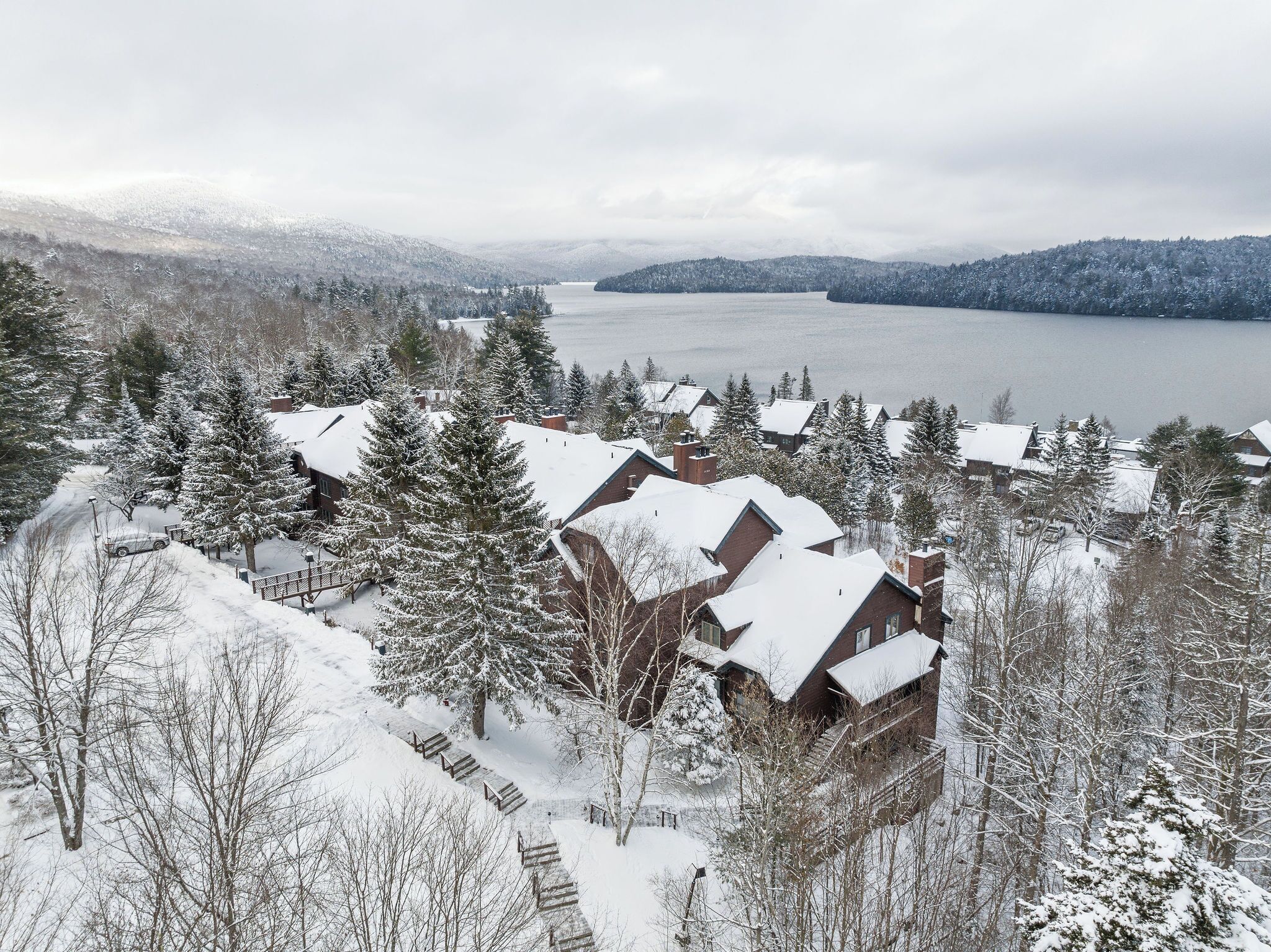 Un quartier résidentiel enneigé, avec des maisons et un lac en arrière-plan.