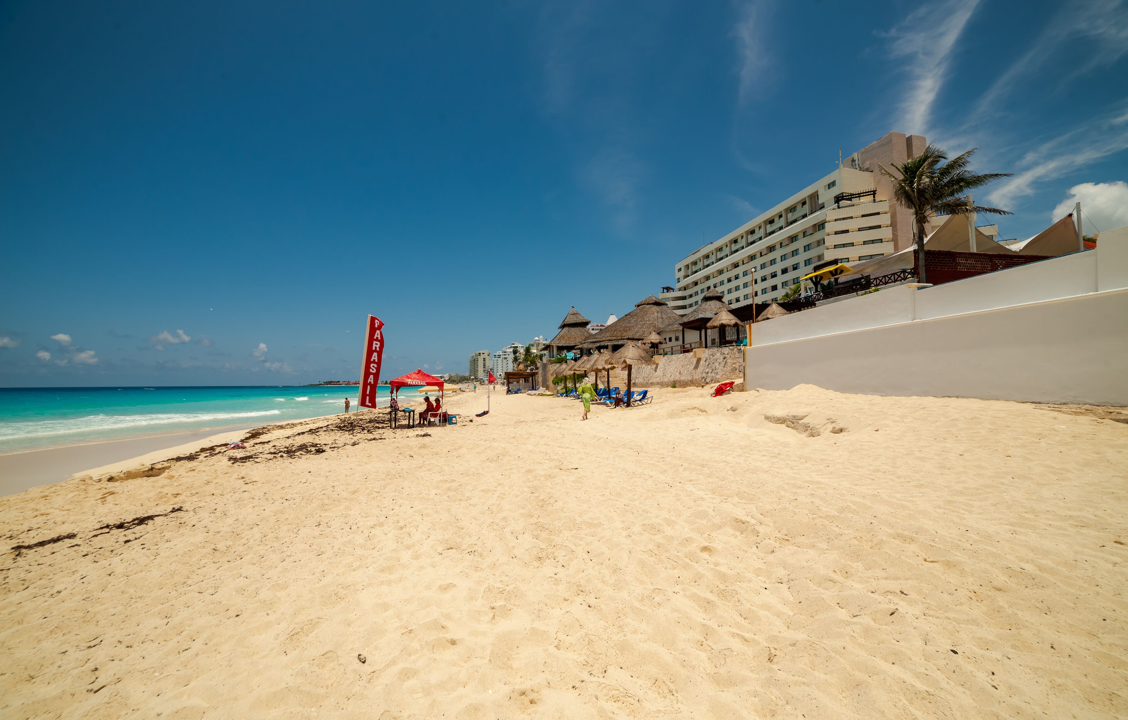 A beach with a hotel in the background, a lifeguard tower, and beach umbrellas.