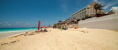 A beach with a hotel in the background, a lifeguard tower, and beach umbrellas.