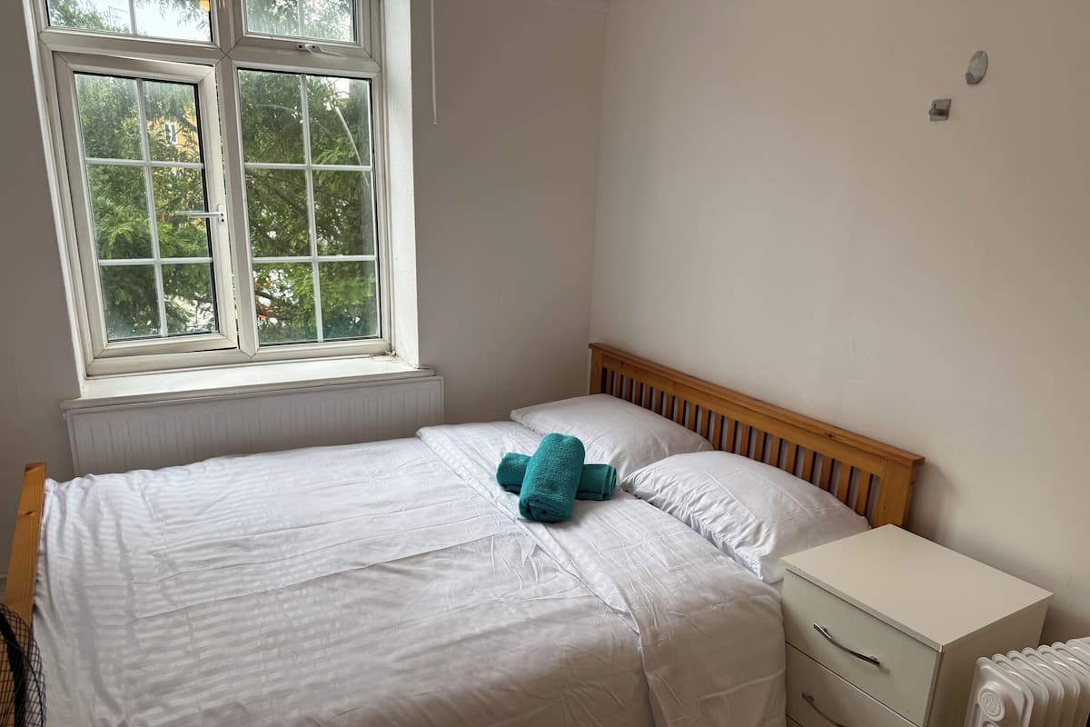 A bedroom with a bed, a nightstand, a radiator, and a window with a view of trees.