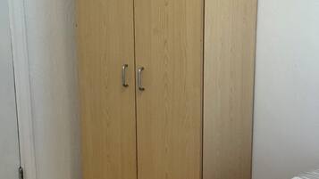 Een slaapkamer met een houten garderobe, een radiator, en een keurig opgevouwen witte handdoek op het bed.